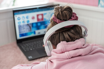 dziewczyna w różowej bluzie i białych słuchawkach, tyłem przed ekranem monitora